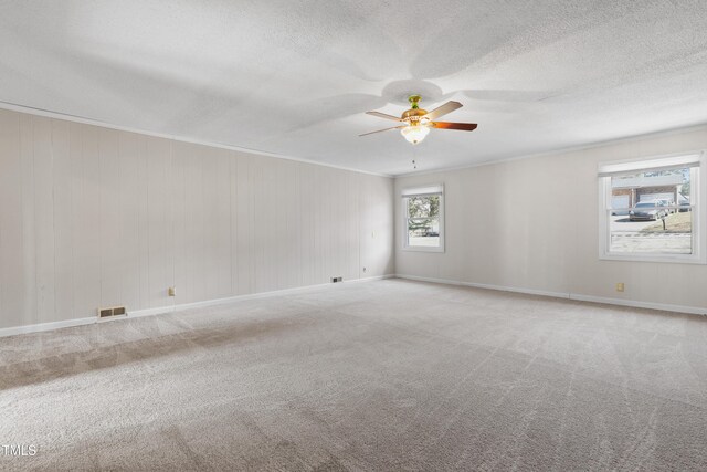 carpeted empty room featuring a textured ceiling, ceiling fan, visible vents, baseboards, and crown molding