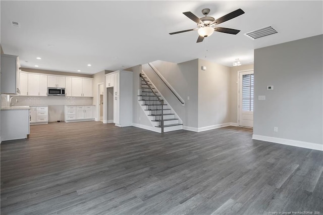 unfurnished living room with dark wood-style floors, baseboards, stairs, and visible vents