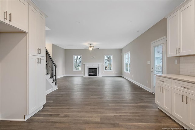 unfurnished living room featuring ceiling fan, a fireplace, dark wood finished floors, and baseboards