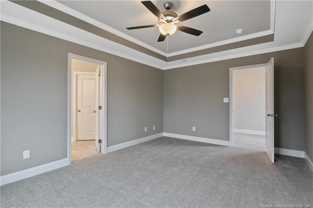 empty room featuring ornamental molding, a tray ceiling, light carpet, and baseboards