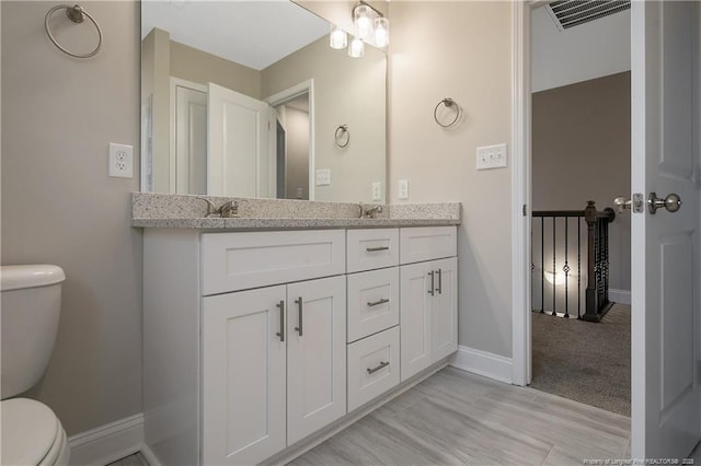 bathroom with toilet, baseboards, double vanity, and visible vents