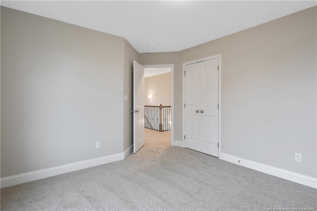 unfurnished bedroom with a closet, light colored carpet, and baseboards