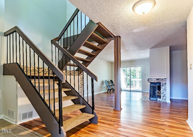 stairway with a tile fireplace, visible vents, baseboards, and wood finished floors