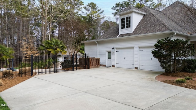 view of side of home with driveway, a shingled roof, an attached garage, and fence