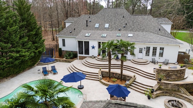 back of property featuring fence, a fire pit, roof with shingles, and a patio area