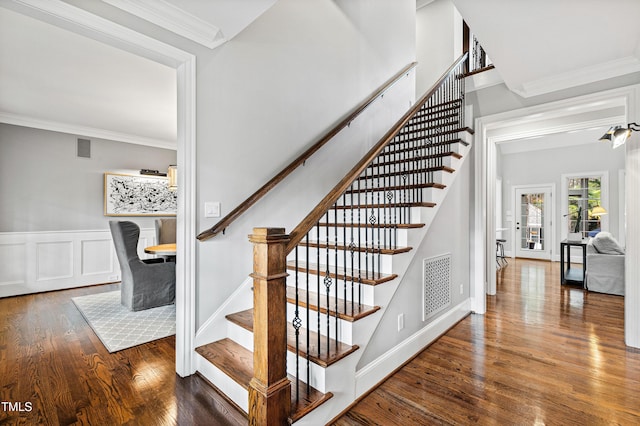 staircase with wood finished floors, a wainscoted wall, visible vents, ornamental molding, and a decorative wall