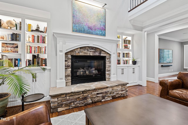 living area with a stone fireplace, crown molding, baseboards, and wood finished floors