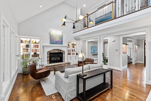 living area featuring baseboards, built in shelves, a stone fireplace, and hardwood / wood-style flooring