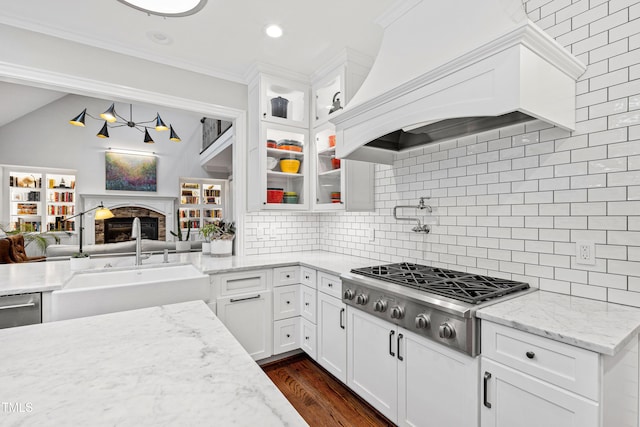 kitchen featuring glass insert cabinets, stainless steel gas cooktop, custom range hood, decorative backsplash, and a sink