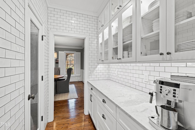 kitchen featuring glass insert cabinets, light stone countertops, ornamental molding, white cabinets, and dark wood-style flooring