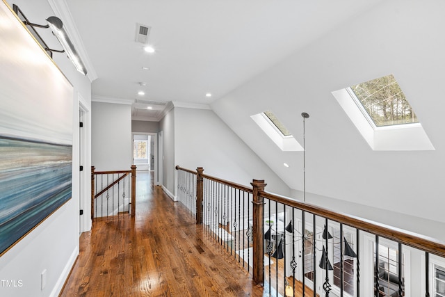 hall with visible vents, an upstairs landing, lofted ceiling with skylight, ornamental molding, and wood finished floors