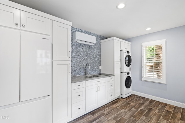 clothes washing area featuring a sink, wood finish floors, a wall mounted AC, and stacked washing maching and dryer