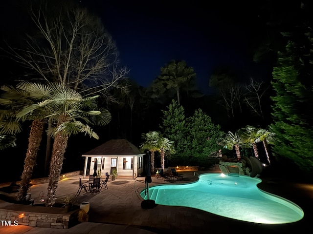 pool at twilight with an exterior structure, an outdoor pool, a patio, and an outbuilding