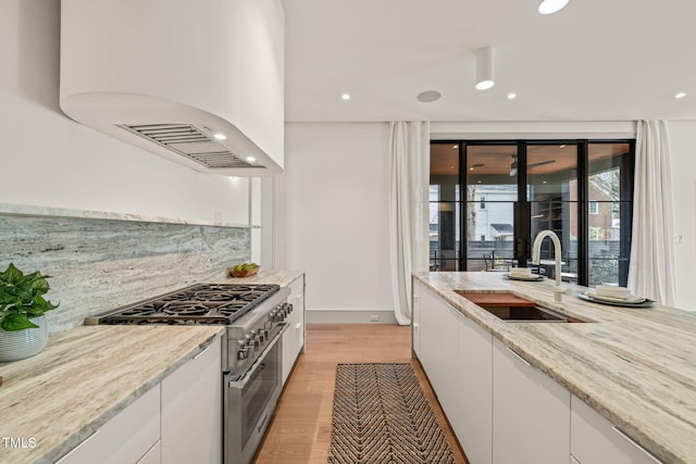 kitchen featuring custom range hood, white cabinetry, high end range, and a sink