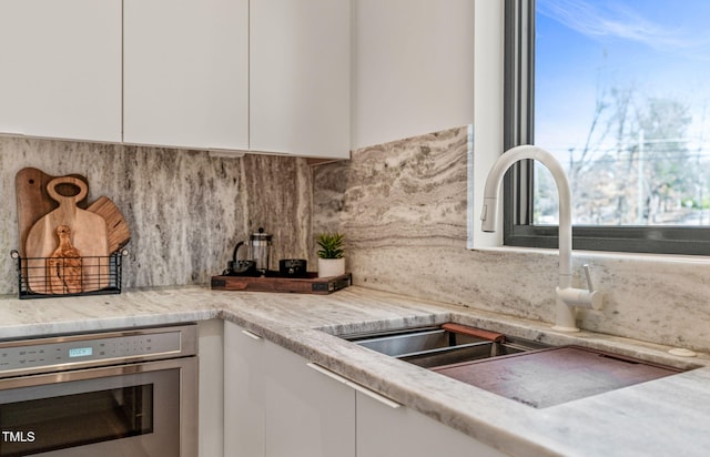 kitchen with stainless steel oven, white cabinetry, a sink, and decorative backsplash