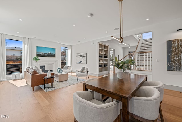 dining space featuring recessed lighting, stairway, light wood-style floors, a glass covered fireplace, and baseboards