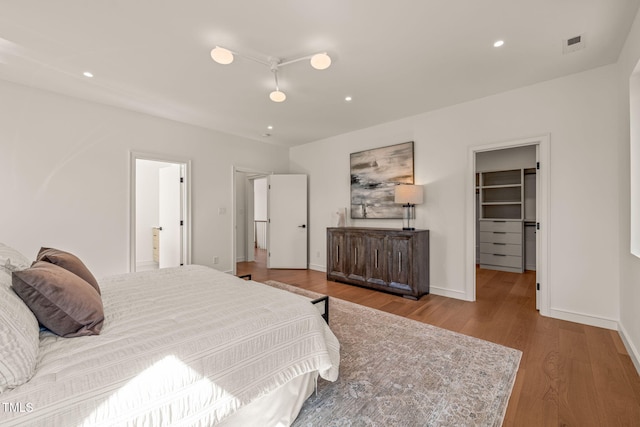 bedroom featuring baseboards, a walk in closet, wood finished floors, and recessed lighting