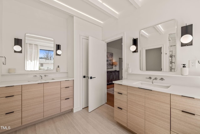 full bath with beam ceiling, two vanities, a sink, and wood finished floors