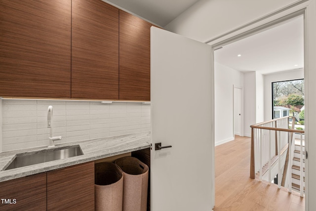 kitchen featuring light stone counters, a sink, light wood-style floors, decorative backsplash, and modern cabinets