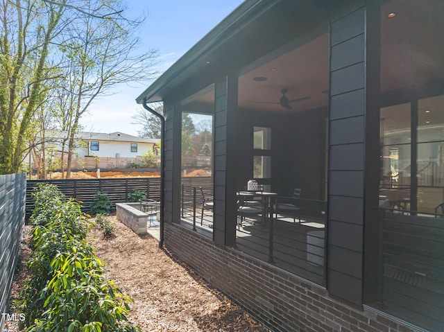 view of side of property with a sunroom, ceiling fan, fence, and brick siding