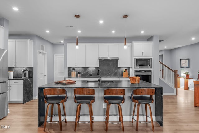 kitchen with light wood finished floors, appliances with stainless steel finishes, white cabinetry, a sink, and under cabinet range hood