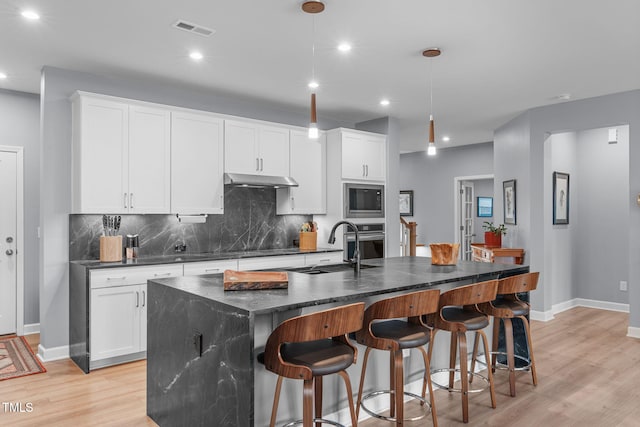 kitchen with built in microwave, under cabinet range hood, stainless steel oven, visible vents, and decorative backsplash