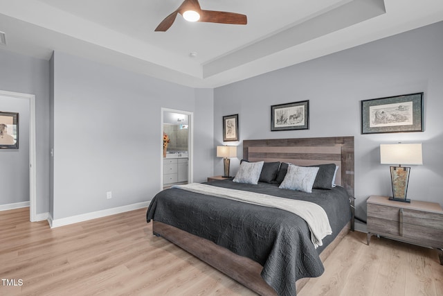 bedroom with a raised ceiling, connected bathroom, baseboards, and wood finished floors