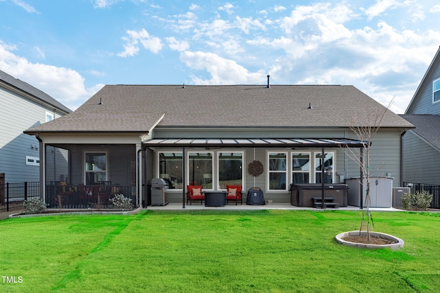 rear view of property featuring a hot tub, a lawn, roof with shingles, fence, and a patio area