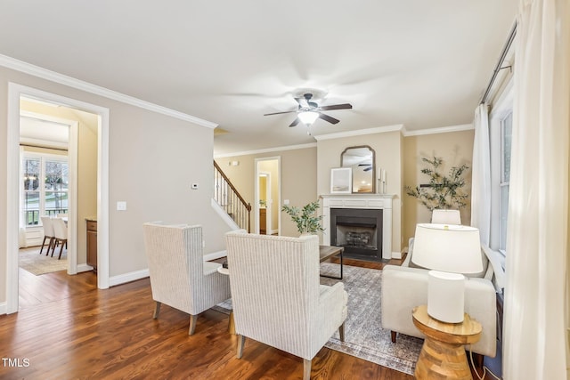 living room featuring crown molding, dark wood-type flooring, a fireplace with flush hearth, baseboards, and stairs