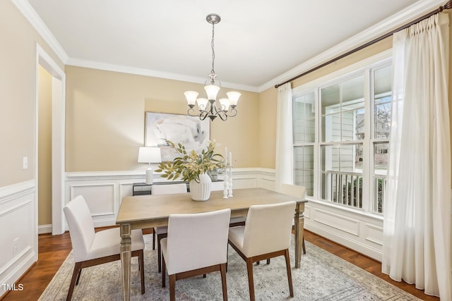 dining room with an inviting chandelier, ornamental molding, a decorative wall, and wood finished floors