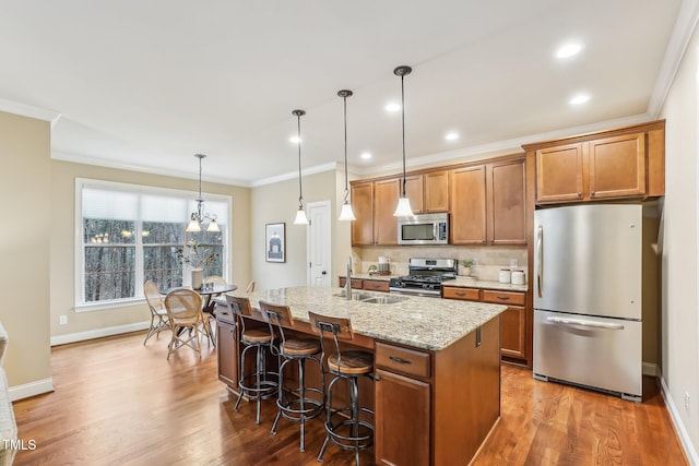 kitchen featuring a kitchen island with sink, stainless steel appliances, a sink, ornamental molding, and brown cabinets