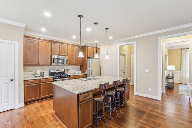 kitchen with brown cabinetry, appliances with stainless steel finishes, a sink, a kitchen island with sink, and backsplash