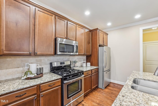 kitchen featuring light wood-style flooring, a sink, ornamental molding, appliances with stainless steel finishes, and backsplash