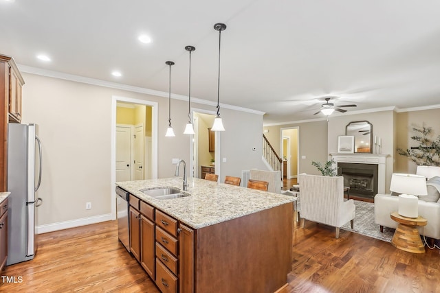 kitchen featuring brown cabinets, a fireplace, light wood finished floors, appliances with stainless steel finishes, and a sink