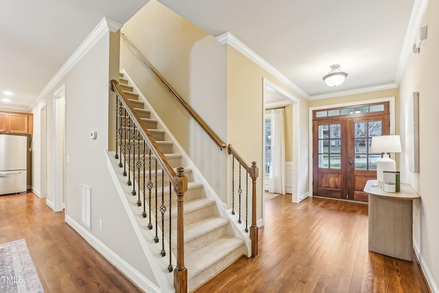 foyer with crown molding, visible vents, light wood-style flooring, baseboards, and stairs