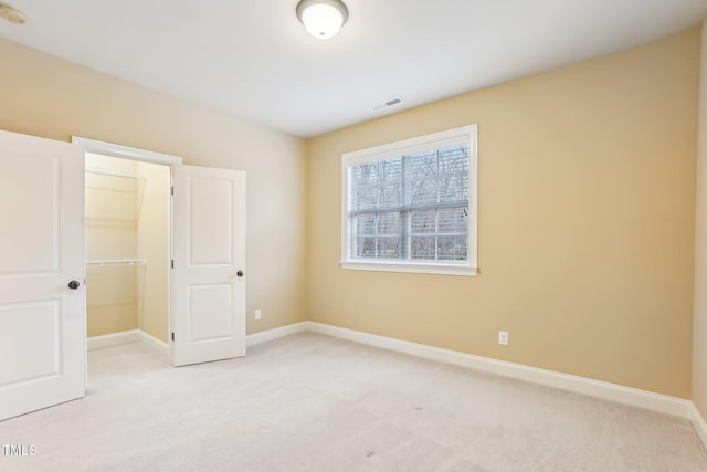 unfurnished bedroom with baseboards, a spacious closet, visible vents, and light colored carpet