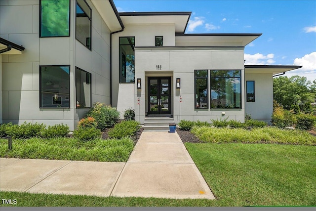 view of exterior entry with french doors, a lawn, and stucco siding