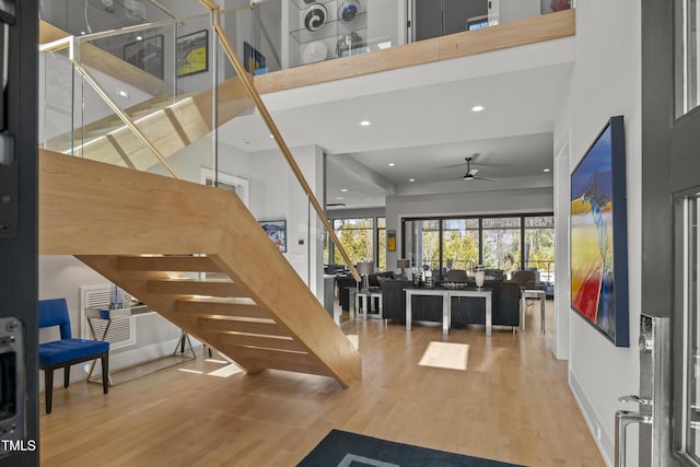 foyer with wood finished floors, stairs, ceiling fan, and a towering ceiling