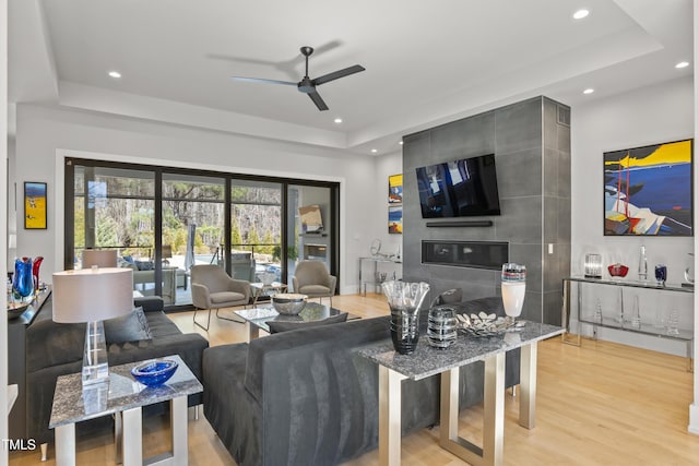 living room with a raised ceiling, recessed lighting, light wood-type flooring, and ceiling fan