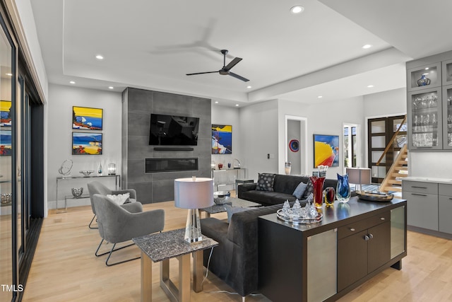 living area featuring light wood finished floors, indoor bar, a tray ceiling, recessed lighting, and a ceiling fan