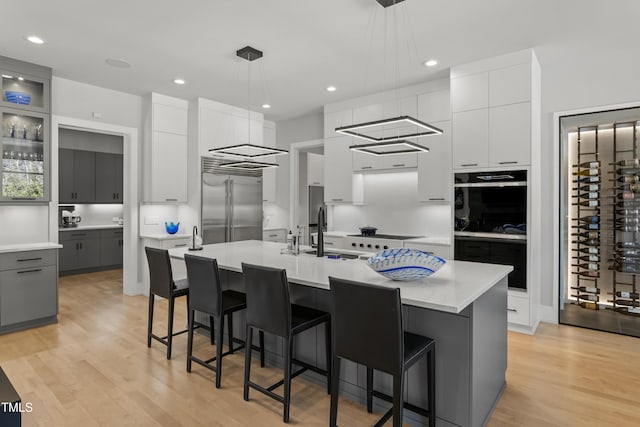 kitchen with modern cabinets, an island with sink, light wood-style flooring, built in fridge, and light countertops