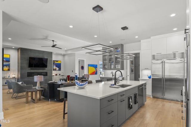 kitchen featuring gray cabinetry, an island with sink, white cabinets, stainless steel appliances, and a sink