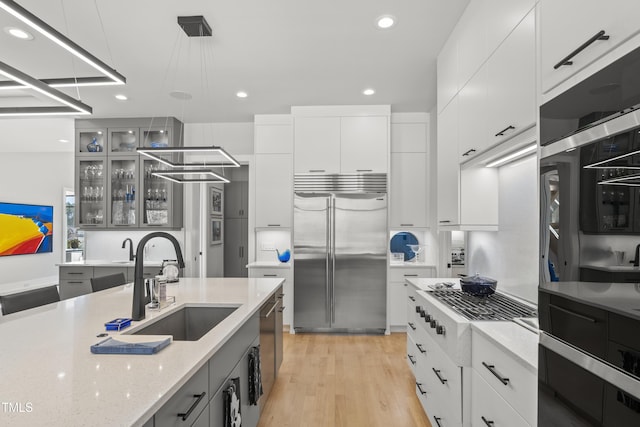 kitchen with light wood-type flooring, stainless steel built in refrigerator, a sink, glass insert cabinets, and hanging light fixtures