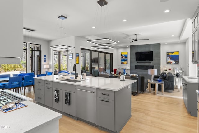 kitchen featuring light wood-type flooring, gray cabinetry, a center island with sink, a sink, and ceiling fan