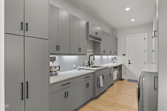 kitchen with tasteful backsplash, light countertops, gray cabinets, light wood-style floors, and a sink