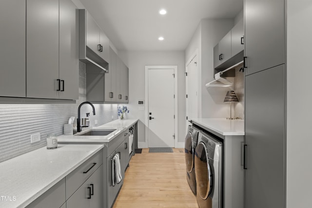 kitchen with gray cabinetry, washer and clothes dryer, a sink, light wood finished floors, and decorative backsplash