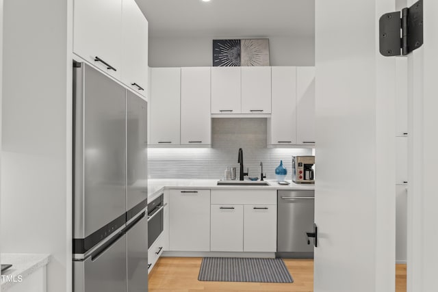 kitchen with a sink, light countertops, appliances with stainless steel finishes, light wood-type flooring, and backsplash