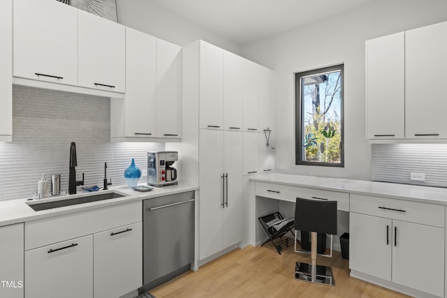 kitchen featuring white cabinetry, a sink, decorative backsplash, dishwasher, and light wood-type flooring