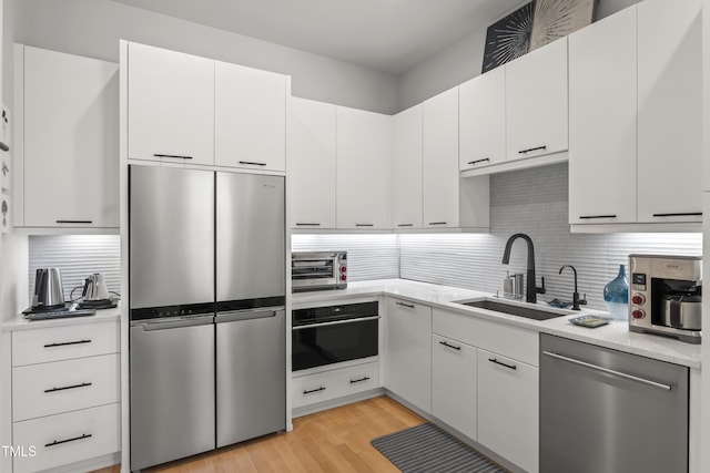 kitchen with light wood-style flooring, a toaster, a sink, stainless steel appliances, and backsplash