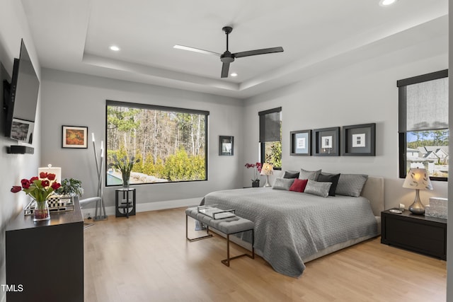 bedroom with recessed lighting, multiple windows, a raised ceiling, and wood finished floors